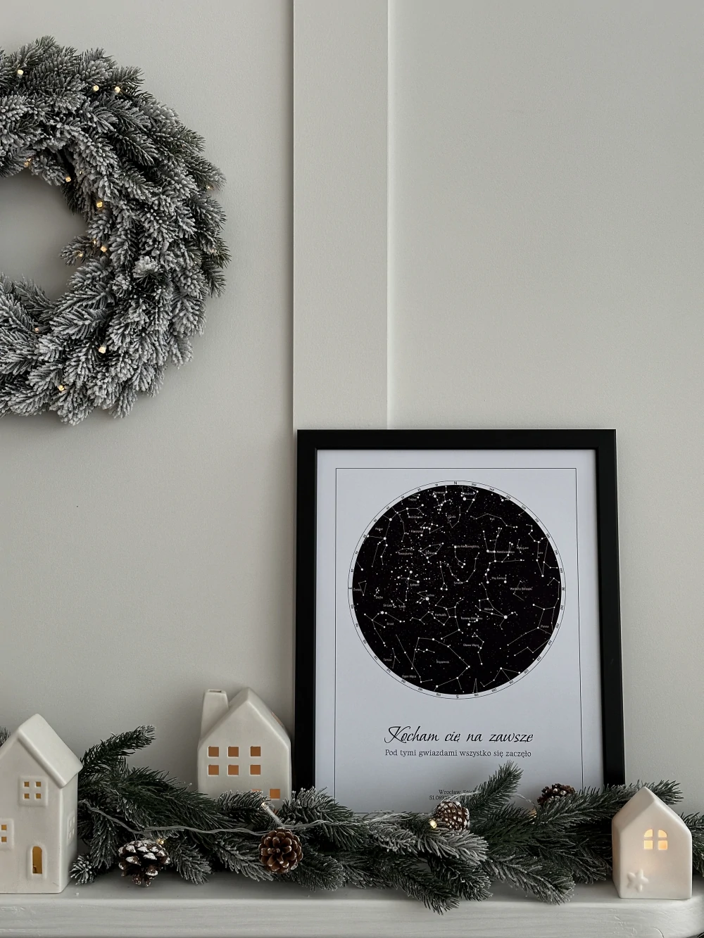 Elegancki prezent dla rodziców na święta w czarnej ramie, stojący na kominku w otoczeniu świątecznych dekoracji.